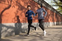 Deportivo joven asiático pareja sonriendo cada otro y jogging juntos en calle - foto de stock