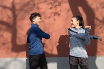 Young male and female athletes in sportswear smiling each other while stretching together on street — Stock Photo