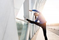 Beautiful happy young woman in sportswear stretching on bridge in the morning — Stock Photo