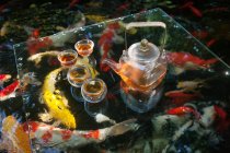 Крупним планом чайний набір, який подається на скляній поверхні в ставку з золотою рибою — стокове фото