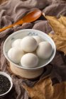 Glutinous rice balls in bowl, wooden spoon, sesame seeds and dry leaves on table — Stock Photo
