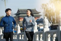 Sporty young couple smiling each other and running together on street — Stock Photo