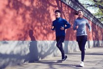 Jovem casal esportivo sorrindo e correndo juntos na rua — Fotografia de Stock