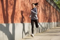 Красивая улыбающаяся азиатка в спортивной одежде бегает по улице — стоковое фото