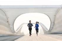 Спортивная молодая пара улыбается друг другу и бегает вместе по мосту — стоковое фото