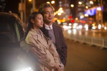 Feliz asiático pareja de pie cerca de coche en la noche - foto de stock