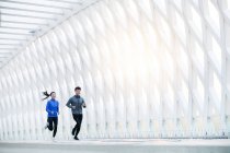Lächelnde junge asiatische Läufer beim gemeinsamen Sportkleidungstraining auf der Brücke — Stockfoto