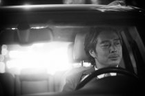 Vista a través del parabrisas de hombre asiático maduro conduciendo coche, imagen en blanco y negro - foto de stock
