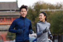 Front view of smiling young asian couple jogging together on street — Stock Photo