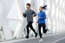 Улыбающаяся спортивная молодая азиатская пара бегает вместе и смотрит вдаль — стоковое фото