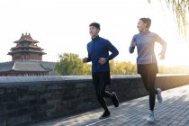 Smiling young male and female chinese athletes in sportswear running together outdoor — Stock Photo