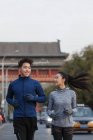 Jóvenes atletas asiáticos en ropa deportiva sonriendo unos a otros y corriendo juntos en la calle - foto de stock