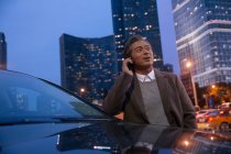 Зрілий азіатський чоловік спирається на машину і розмовляє по смартфону в нічному місті — стокове фото
