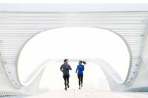 Young couple in sportswear running on bridge and looking at each other — Stock Photo