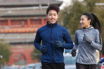 Jovem ásia casal no sportswear sorrindo e correndo juntos no rua — Fotografia de Stock