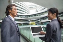 Asian businesspeople walking with laptop in modern business center — Stock Photo