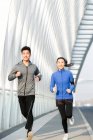 Vista frontal de jóvenes atletas asiáticos en ropa deportiva corriendo y sonriendo a la cámara en el puente - foto de stock