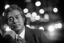 Retrato de guapo maduro asiático hombre mirando cámara en noche ciudad, blanco y negro imagen - foto de stock