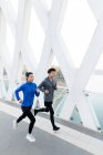 Blick aus der Vogelperspektive auf lächelnde junge asiatische Athleten, die zusammen auf einer Brücke laufen — Stockfoto