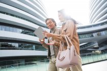 Smiling businesspeople walking and using tablet near modern business center — Stock Photo