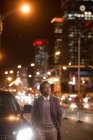 Maturo asiatico uomo in piedi con le mani in tasche accanto auto e guardando lontano in notte città — Foto stock