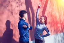Happy young asian couple in sportswear smiling each other and stretching together on street in the morning — Stock Photo