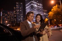 Felice coppia asiatica guardando tablet vicino auto alla sera — Foto stock