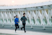 Sorrindo jovem asiático homem e mulher no sportswear correndo juntos na ponte — Fotografia de Stock