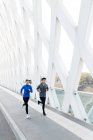 Высокий угол обзора улыбающихся молодых бегунов, бегущих по мосту — стоковое фото