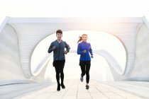 Young asian male and female athletes in sportswear jogging together on modern bridge — Stock Photo