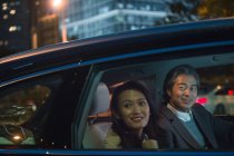 Счастливая азиатская пара, едущая в машине и глядя в окно вечером — стоковое фото