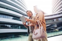Cheerful businesspeople walking and using tablet near modern business center — Stock Photo