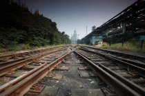 Залізниця з залізничними коліями між промисловим будівництвом і зеленими деревами — стокове фото
