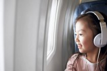 Adorable niño feliz en los auriculares sentado en el avión y mirando a la ventana - foto de stock