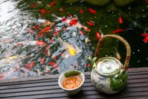 Vista de ángulo alto del juego de té y peces de colores nadando en el estanque - foto de stock