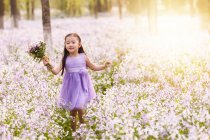 Adorable asian kid in dress walking with bouquet of flowers in field — Stock Photo
