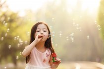 Adorable asian kid blowing soap bubbles near railroad — Stock Photo