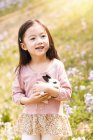 Entzückendes asiatisches Kind im Kleid mit Kaninchen auf dem Blumenfeld — Stockfoto