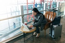 Hermosa joven empresaria utilizando el ordenador portátil y teléfono inteligente en el salón del aeropuerto - foto de stock