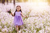 Чарівна азіатська дитина в сукні, що йде з букетом квітів у полі — стокове фото
