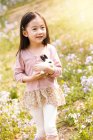 Чарівна азіатська дитина в сукні тримає кролика на квітковому полі — стокове фото