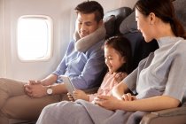 Glückliche Familie mit einem Kind, das mit dem Flugzeug reist und ein digitales Tablet nutzt — Stockfoto