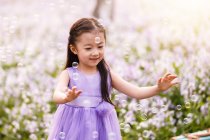 Entzückende asiatische Kind im Kleid fangen Seifenblasen auf Blumenfeld — Stockfoto