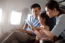 Famille heureuse avec un enfant voyageant en avion et utilisant une tablette numérique — Photo de stock