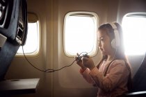 Visão lateral de adorável menina em fones de ouvido jogando jogos por gamepad no avião — Fotografia de Stock