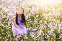 Adorable asian kid in dress sitting on bag at flower field — Stock Photo