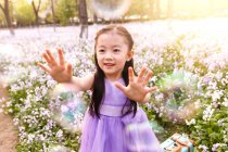 Adorable asiático niño en vestido captura jabón burbujas en flor campo - foto de stock