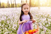 Adorable asian kid in dress holding basket with easter eggs at flower field — Stock Photo