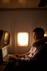Young man using laptop while sitting in plane, side view — Stock Photo
