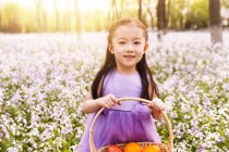 Чарівна азіатська дитина в сукні тримає кошик з великодніми яйцями на квітковому полі — стокове фото
